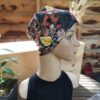 Un mannequin aux traits réalistes porte le Bonnet Catherine (sans bandeau), un foulard coloré orné de motifs floraux et papillons.